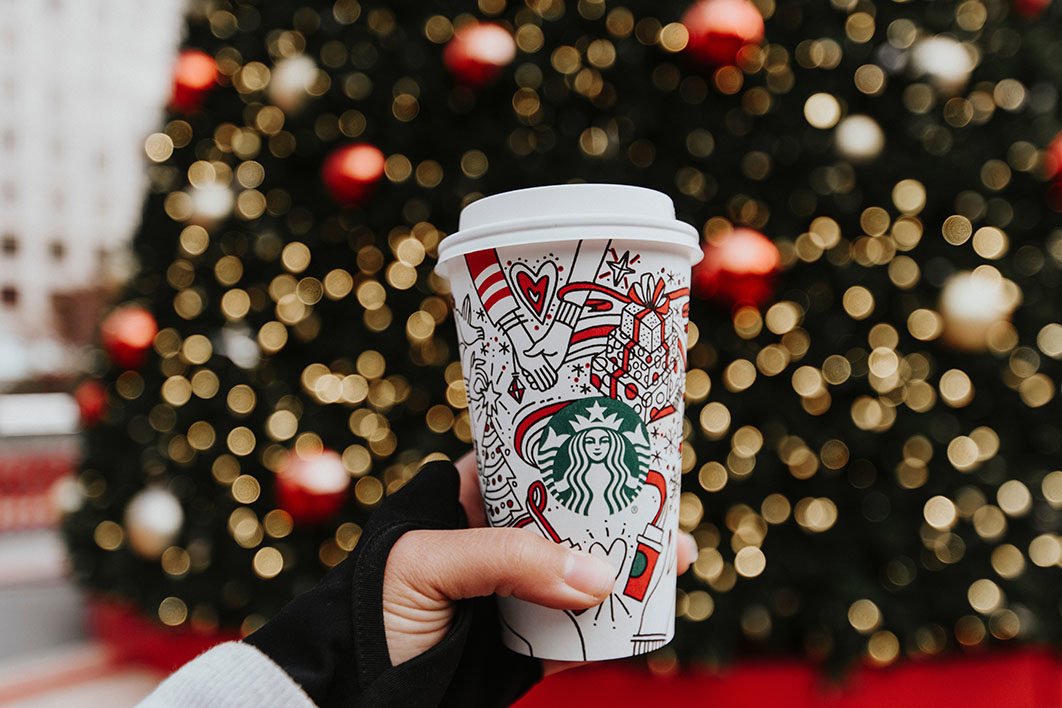 person holding white Starbucks cup in front of Christmas tree